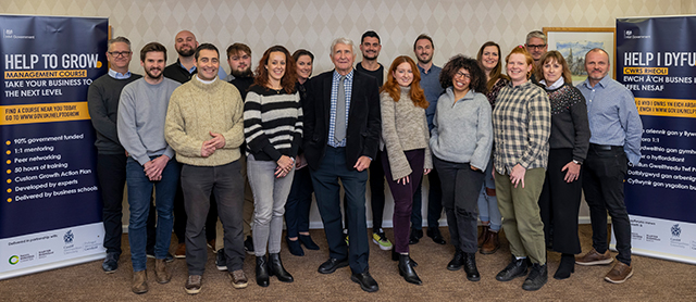 Photo of the whole cohort of the Help to Grow next cohort and two banners advertising the Help to Grow either side(one in Welsh, one in English)